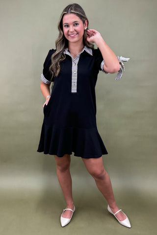 Woman wearing a black dress with white accents against a plain background