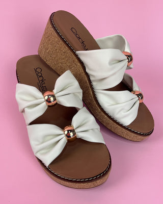 White sandals with brown soles and decorative bows on a pink background