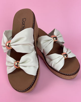 Brown sandals with white bow straps on a pink background