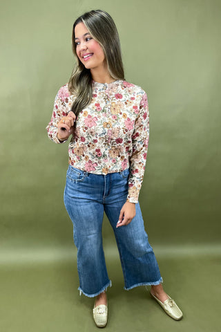Woman wearing a floral top and blue jeans against a green background