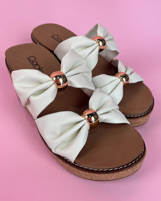 White sandals with brown soles and decorative bows on a pink background