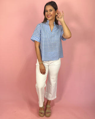 Woman wearing a blue checkered shirt and white pants against a pink background