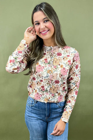 Woman wearing a floral long-sleeve top and blue jeans against a green background