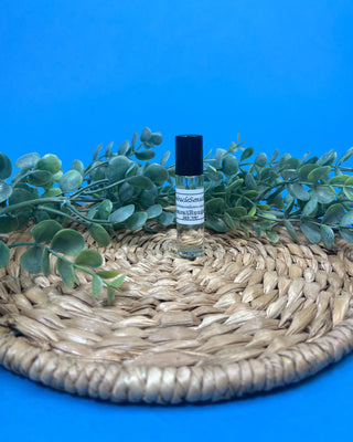 A small clear glass rollerball bottle with a white label and '100% Organic', shown on a wooden surface with a black cap beside it and a blue background.