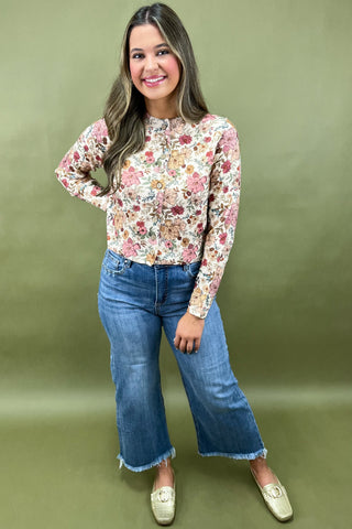 Woman wearing a floral blouse and blue jeans against a green background