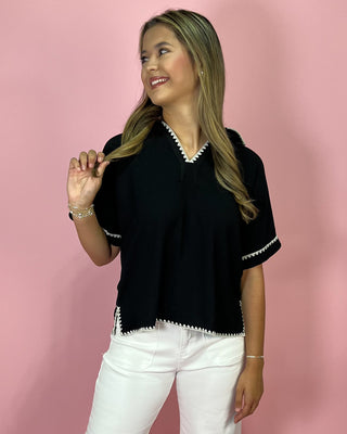 Woman wearing a black top with white trim against a pink background