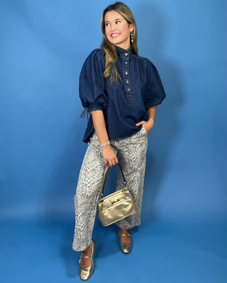 wearing a dark navy blue puff-sleeve blouse with a buttoned high collar, patterned gray and white snakeskin print pants,