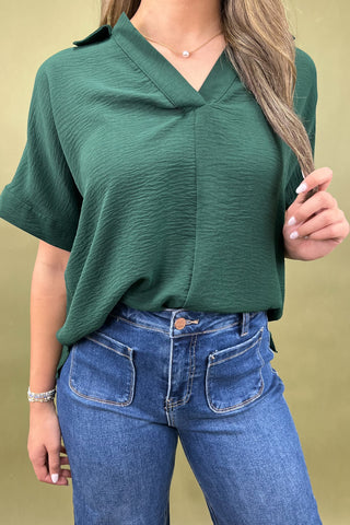 Person wearing a green top and blue jeans against a beige background