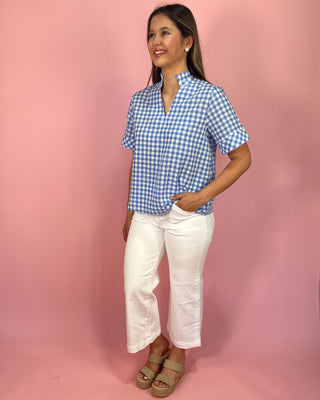 Woman wearing a blue checkered shirt and white pants against a pink background
