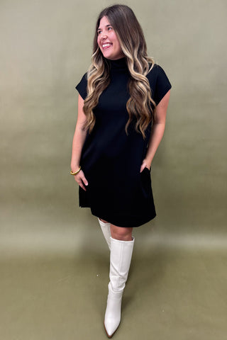 Woman wearing a black dress and white knee-high boots against a green background