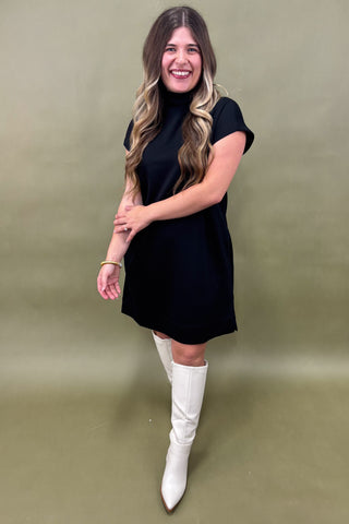 Woman wearing a black dress and white knee-high boots against a green background