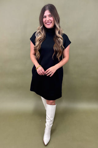 Woman wearing a black dress and white knee-high boots against a green background