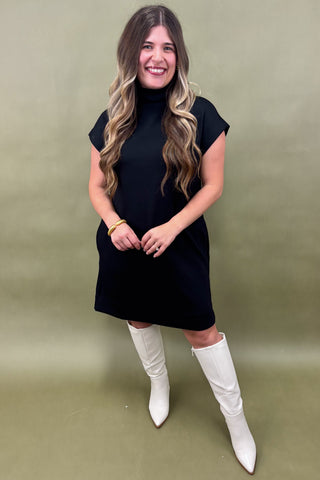 Woman wearing a black dress and white knee-high boots against a green background