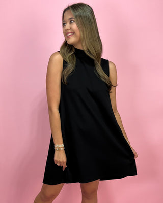 Woman wearing a black sleeveless dress against a pink background