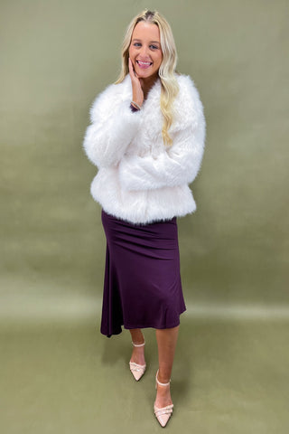 Woman wearing a white fur coat and purple skirt against a green background