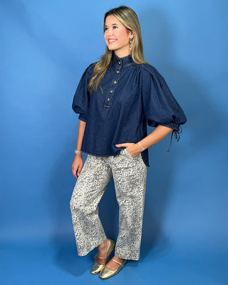 A woman modeling a dark indigo blue puff-sleeve blouse with a button placket and high collar, paired with wide-leg patterned pants