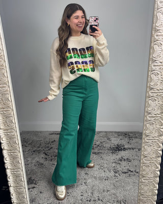 Woman taking a mirror selfie wearing a colorful sweater and green pants.