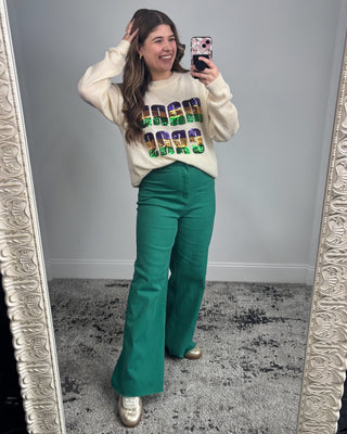 Person taking a mirror selfie wearing a colorful sweater and green pants.