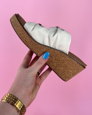 Hand holding a cork sandal with white cushioned insole against a pink background