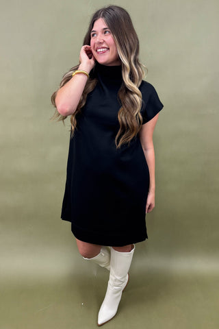 Woman wearing a black dress and white knee-high boots against a green background