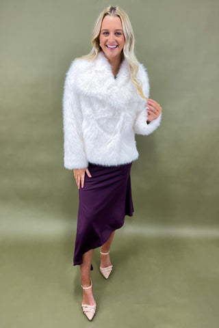 Woman wearing a white fluffy jacket and purple skirt on a green background