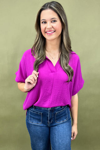 Woman wearing a bright pink top and blue jeans against a green background