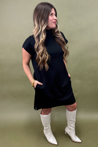 Woman wearing a black dress and white knee-high boots against a green background