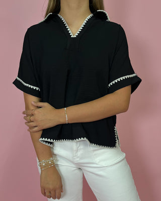 Person wearing a black top with white trim against a pink background
