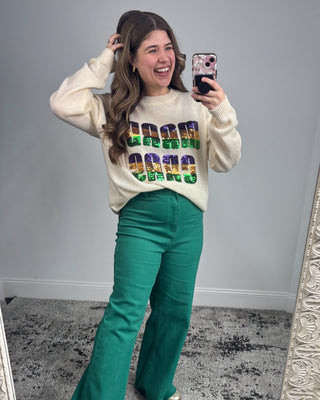 Woman wearing a colorful sweater and green pants taking a mirror selfie.