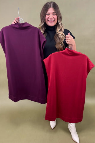 Woman holding two dresses, one purple and one red, against a green background