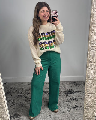 Woman taking a mirror selfie wearing a colorful sweater and green pants.