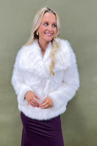 Woman wearing a white fur shrug against a green background