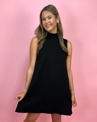 Woman wearing a black sleeveless dress against a pink background