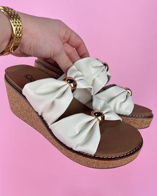 White sandals with bow details on a pink background