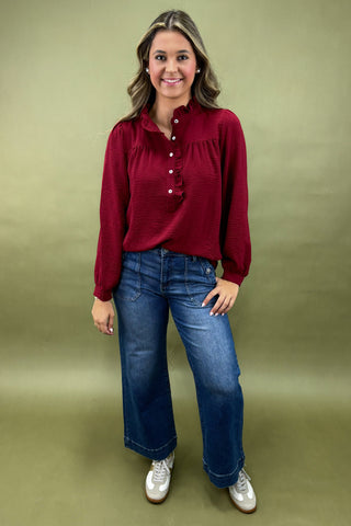 Woman wearing a red blouse and blue jeans against a green background