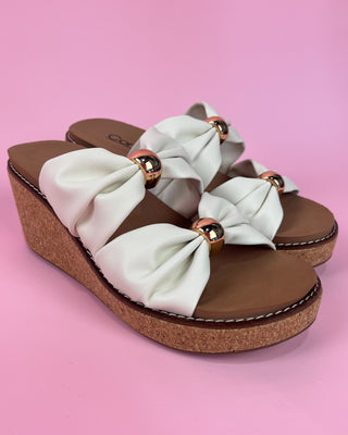 Wedge sandals with white bows and brown soles on a pink background