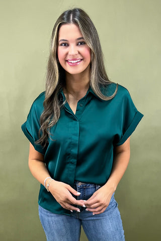 Woman wearing a teal blouse and blue jeans against a green background
