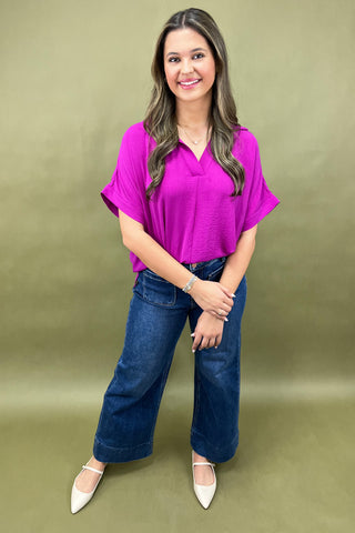 Woman wearing a purple top and blue jeans against a green background