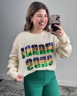 Person wearing a sweater with colorful sequin letters, taking a selfie.
