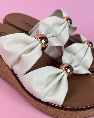 White sandals with gold accents on a pink background