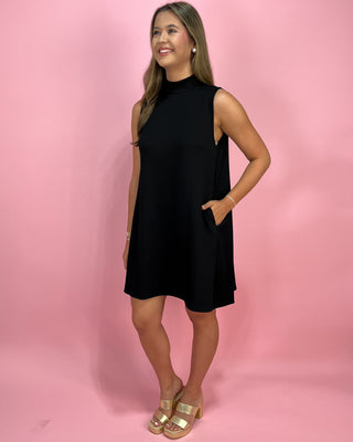 Woman wearing a black sleeveless dress against a pink background