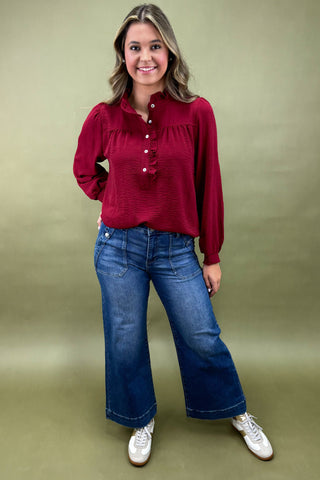 Woman wearing a red blouse and blue jeans against a green background