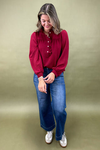 Woman wearing a red blouse and blue jeans against a beige background