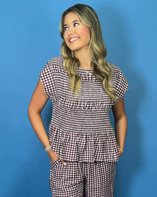A woman modeling a matching two-piece gingham set consisting of a short-sleeve peplum top and coordinating pants