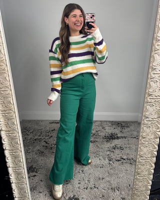 Person wearing a colorful striped sweater and green pants standing in front of a mirror.