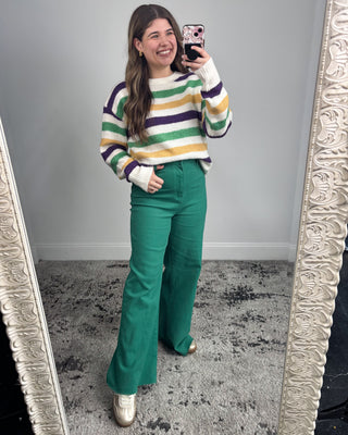 Person wearing a striped sweater and green pants taking a mirror selfie.