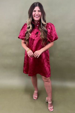 Woman wearing a red dress with puffed sleeves against a green background