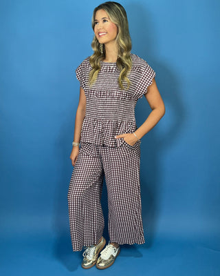 A woman modeling a matching two-piece set consisting of a short-sleeve ruffled peplum top and wide-leg pants in a small black and white gingham pattern
