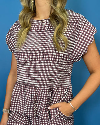 A woman wearing a smocked short-sleeve top with a brown and white gingham pattern