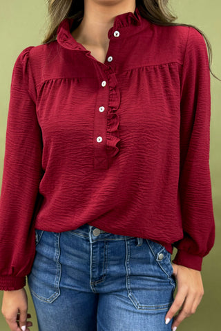Red blouse with ruffled details worn by a person against a green background